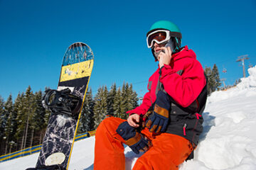 Low angle shot of a snowboarder resting sitting on the slope talking on the phone technology communication carrier sportsman seasonal activity winter resort Bukovel