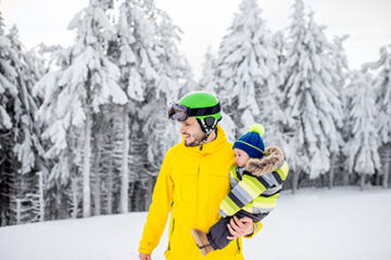 Man in colorful sports clothes riding the snowboard on the snowy mountains with beautiful trees on the background